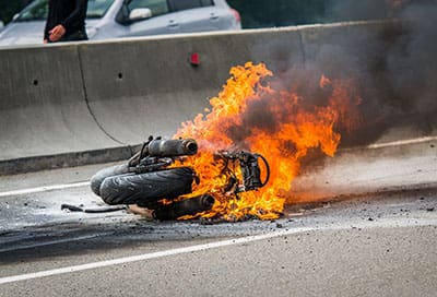 The wreckage of a motorbike on fire at the side of a freeway after an accident