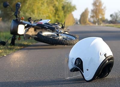A helmet lying in the street next to a crashed motorcycle